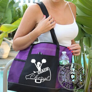 May include: Purple and black tote bag with a white design of a cheerleader holding pom-poms and a megaphone with the text "COACH Cheryl".