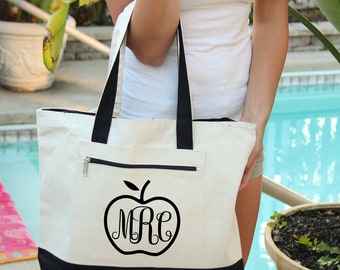 May include: A white canvas tote bag with black trim and a black apple design featuring the monogram "MRE".