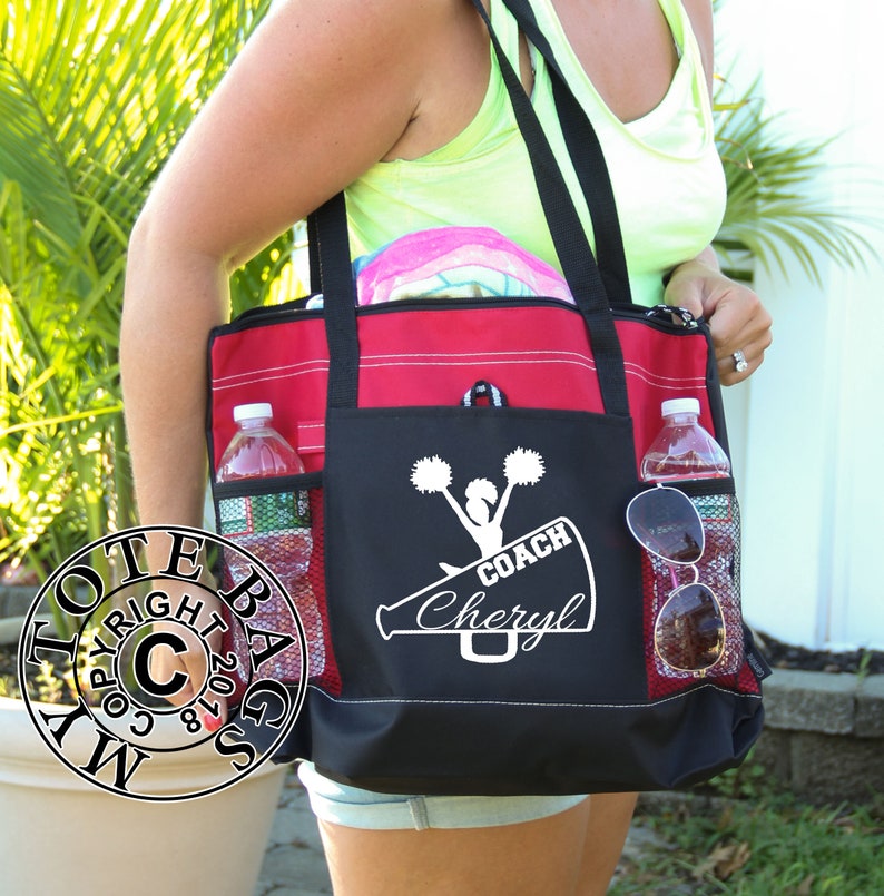 May include: A black and red tote bag with a white design of a cheerleader holding pom-poms and a megaphone with the text "COACH Cheryl".