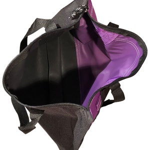 May include: Purple and black tote bag with a zipper closure and two handles. The bag is open and the inside is visible.