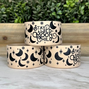 May include: Three beige silicone bracelets with a black and white moon and star pattern. The top bracelet has the text "Stay Wild Moon Child" in a black cursive font.
