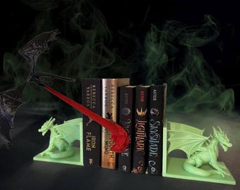 May include: A set of green dragon bookends with a red dragon tail bookend. The bookends are holding up a stack of fantasy novels with titles like "SkyShade", "Lightlark", and "Fourth Wing".