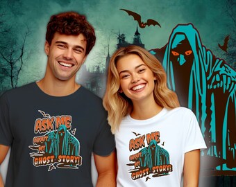 Może przedstawiać: Ciemnoszary t-shirt oraz biały t-shirt, każdy z nadrukiem graficznym przedstawiającym postać w kapturze i niebieskiej pelerynie z pomarańczowymi oczami. Napis "ASK ME ABOUT MY GHOST STORY!" widnieje w pomarańczowo-białych literach wokół postaci.