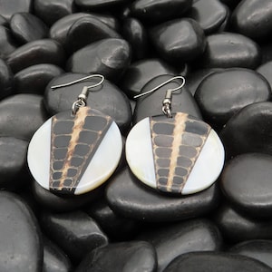 May include: A pair of round, black and white earrings with a geometric design. The earrings are made of shell and have a silver hook.