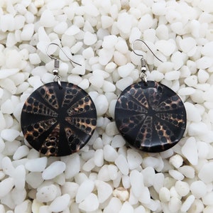 May include: A pair of black and brown earrings with a geometric pattern. The earrings are made of a natural material, possibly shell or wood. The earrings have silver hooks.