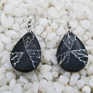 May include: A pair of black teardrop-shaped earrings with a white floral design. The earrings have silver hooks.