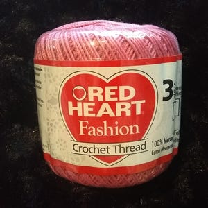 May include: A pink ball of Red Heart Fashion Crochet Thread. The label says "Red Heart Fashion Crochet Thread" and "100% Mercerized Cotton".
