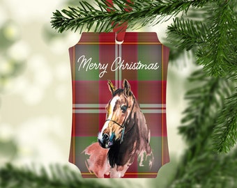 May include: A Christmas ornament featuring a watercolor painting of a brown horse's head on a red and green plaid background. The ornament has a white inscription that reads "Merry Christmas".