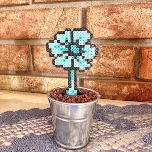 May include: A blue and black beaded flower in a small metal pot with brown beads around the base.