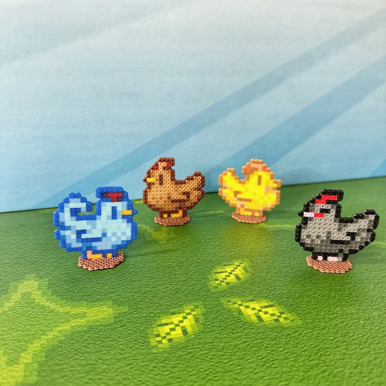 May include: Four pixel art chickens in blue, brown, yellow, and black, each with a red comb. They are arranged on a green surface with a blue background. The chickens are made of small, colorful beads.