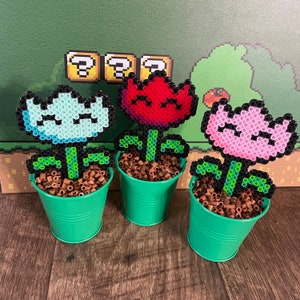May include: Three potted pixel art flowers. The flowers are red, blue, and pink. The pots are green. The flowers are in a pixel art style, with a blocky design.