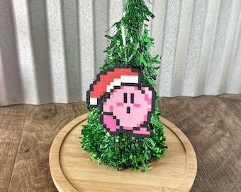 May include: A green Christmas tree with a pink and red pixelated character wearing a Santa hat ornament.