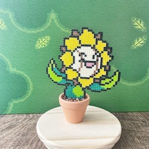 May include: A yellow and green pixel art sunflower with a smiling face, in a brown pot, on a white pedestal.