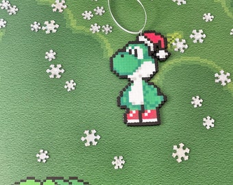 May include: A green and white Christmas ornament featuring a pixelated Yoshi wearing a Santa hat and red boots. The ornament is surrounded by white snowflakes on a green background.