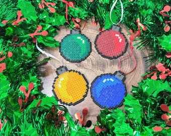 May include: Four colorful Christmas ornaments made of plastic beads. The ornaments are red, blue, green, and yellow. They are arranged on a green and red garland.