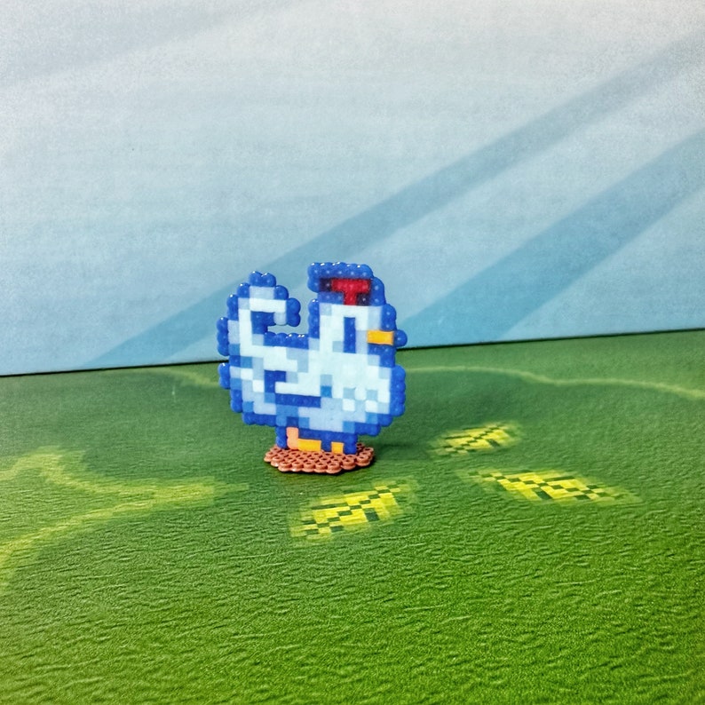 May include: A pixelated chicken figurine in shades of blue, white, red, and yellow. The chicken is standing on a brown base, with a green and blue background. The figurine is a charming, handcrafted item.
