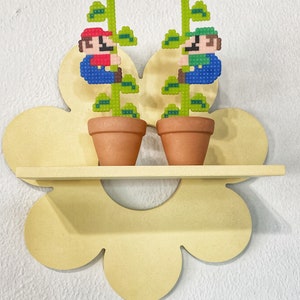 Puede incluir: Dos pequeñas macetas de terracota con plantas verdes y figuras pixeladas de Mario y Luigi trepando por las plantas. Las macetas están en una estantería amarilla con forma de flor.