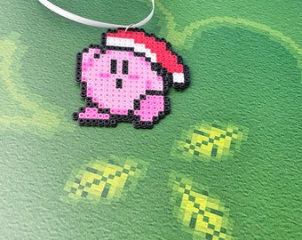 May include: A pink and black pixelated Christmas ornament of a video game character wearing a red and white Santa hat.