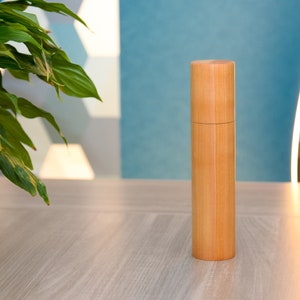 Peut inclure: Un moulin à sel et à poivre en bois naturel de forme cylindrique. Le moulin est en bois brun clair et a une finition lisse.