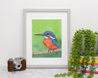 May include: A framed watercolor painting of a kingfisher bird. The bird has blue, orange, and white feathers and is perched on a branch against a green background. The frame is light gray.