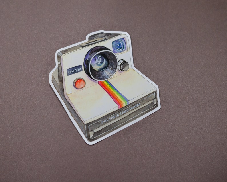 Pu&ograve; includere: Un adesivo di una Polaroid Land Camera in stile vintage con una striscia arcobaleno e il testo "One Step" e "Polaroid Land Camera".