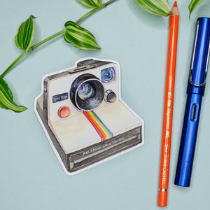 Pu&ograve; includere: Un adesivo con una Polaroid Land Camera in stile vintage con corpo bianco, strisce arcobaleno e il testo "One Step" e "Polaroid Land Camera".