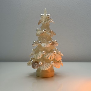 May include: A white seashell Christmas tree with pearl-like ornaments. The tree is made of seashells and has a white base.