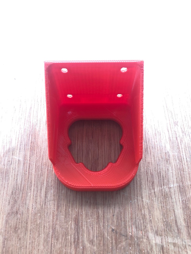 May include: A red 3D printed plastic bracket with four holes for mounting. The bracket has a cutout in the centre.
