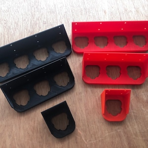 May include: Two black and two red 3D printed wall mounted organisers with three compartments each. There is also a single red 3D printed organiser with one compartment.