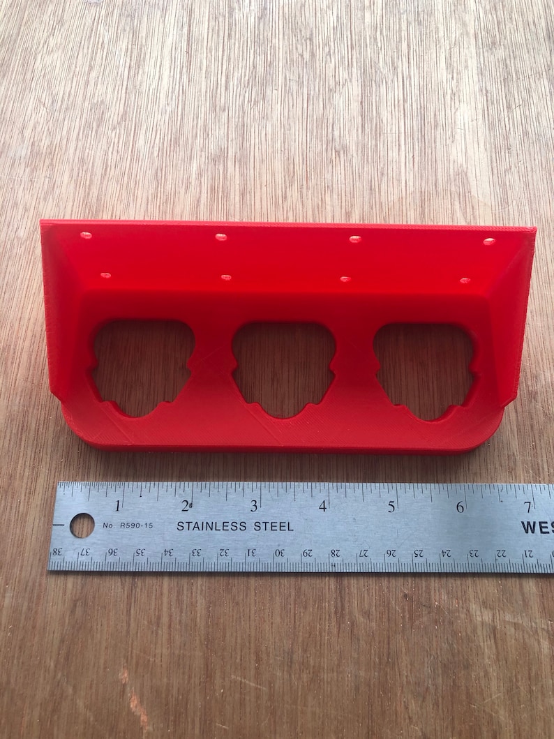 May include: A red plastic 3D printed wall mount with three circular cutouts. The mount is 15 cm long and has a ruler underneath it.