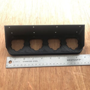 May include: Black metal shelf with four slots for holding items. The shelf is 20 cm long and has a ruler underneath.