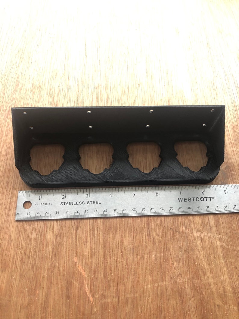 May include: Black metal shelf with four slots for holding items. The shelf is 20 cm long and has a ruler underneath.