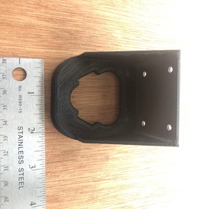 May include: Black plastic 3D printed wall mount with four screw holes and a circular cutout.