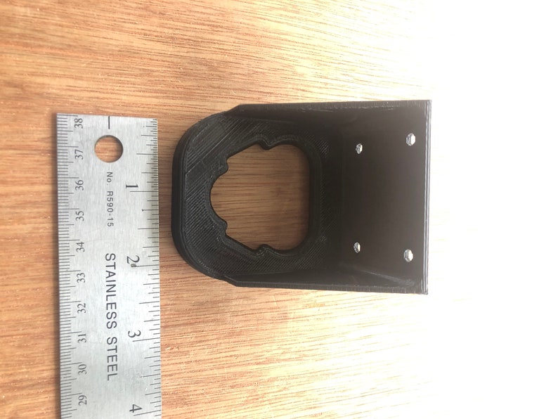 May include: Black plastic 3D printed wall mount with four screw holes and a circular cutout.