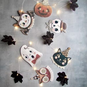 May include: A string of LED fairy lights featuring decorative cutouts of a pumpkin, bat, skull, ghost, black cat, and owl, interspersed with dark fabric maple leaves. Each character wears a small party hat, creating a festive Halloween display.