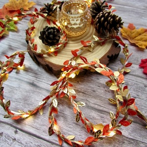 May include: A string of fairy lights with gold and orange leaves, perfect for fall decor. The lights are wrapped around a wooden slice and surrounded by fall leaves.