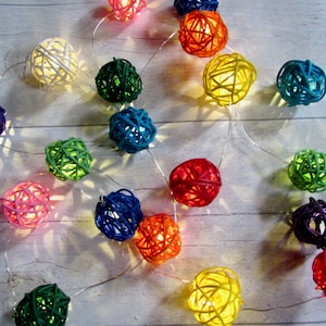 May include: A string of colourful, woven ball lights. The balls are in various colours, including red, orange, yellow, green, blue, purple, and white. The lights are strung on a clear wire and are perfect for adding a touch of whimsy to any room.