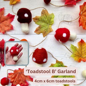 May include: A garland featuring felted toadstools with red and dark red caps with white spots and cream-colored stems, interspersed with artificial autumn leaves on a string. The toadstools measure 4cm x 6cm. Text reads 'Toadstool B' Garland.