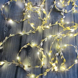 May include: Gold leaf garland with warm white LED lights. The garland is made of artificial leaves and is perfect for decorating for a wedding, party, or holiday.