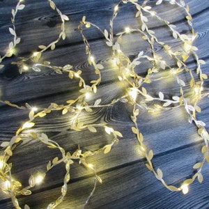 May include: A string of decorative fairy lights featuring metallic gold-coloured leaves interspersed along a thin wire. The lights emit a warm glow, illuminating the individual leaf shapes throughout the length of the flexible wire strand.