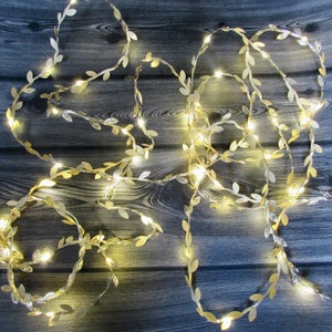 May include: Gold leaf garland with warm white LED lights. The garland is made of artificial leaves and is perfect for decorating for a wedding, party, or holiday.