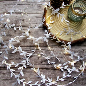May include: White string lights with small white leaves, wrapped around a wooden slice. The lights are on and glowing.