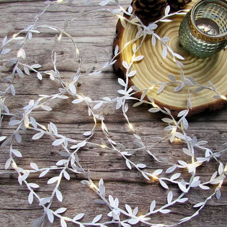 May include: White string lights with small white leaves, wrapped around a wooden slice. The lights are on and glowing.