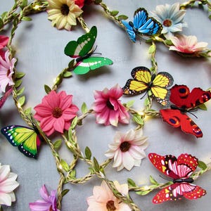 May include: A decorative floral garland with colourful butterflies and flowers. The garland features a woven vine base with pink, yellow, and white flowers, and vibrant butterflies in shades of red, yellow, green, and blue.