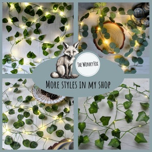 May include: Artificial ivy garland with warm white LED lights. The garland is draped over a wooden surface and a table. The garland is also shown in a close-up view. The text "The Wonky Fox" and "More Styles in My Shop" are visible in the image.