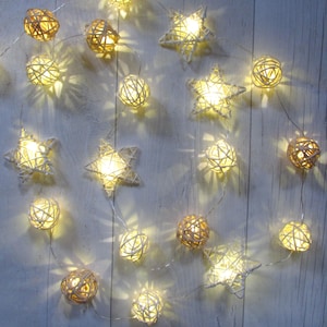 May include: A string of decorative lights featuring woven rattan spheres and star-shaped ornaments. Each piece is illuminated by a warm white LED bulb, connected by a thin, flexible silver wire that creates a glowing effect across the entire arrangement.