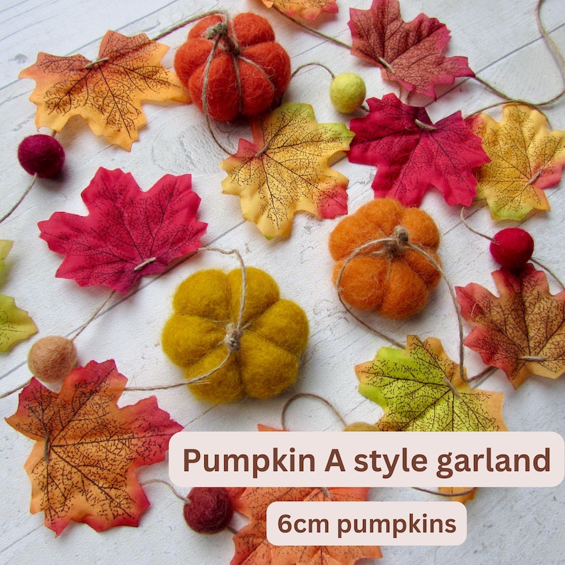May include: A garland featuring felt pumpkins and fabric autumn leaves in shades of red, orange, and yellow. The garland includes 6cm pumpkins and is labeled Pumpkin A style garland. The decorative elements are strung together on a thin twine cord.