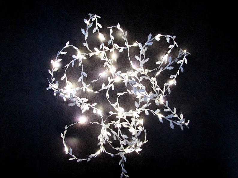 May include: White string lights with small white leaves, arranged in a loose, tangled pattern against a black background.