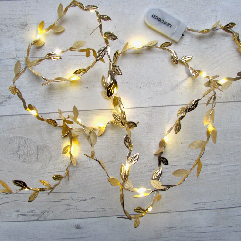 May include: Gold leaf garland with warm white LED lights. The garland is battery operated and has a small remote control.