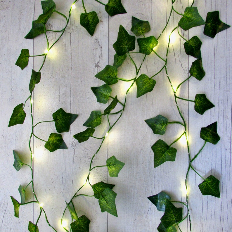 May include: A string of fairy lights wrapped around artificial ivy vines. The lights are white and the ivy is green.